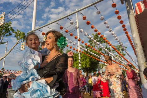 Image of woman carrying a child, both dressed with flamenco dresses at the Seville Fair. Photo by Eduardo Libby