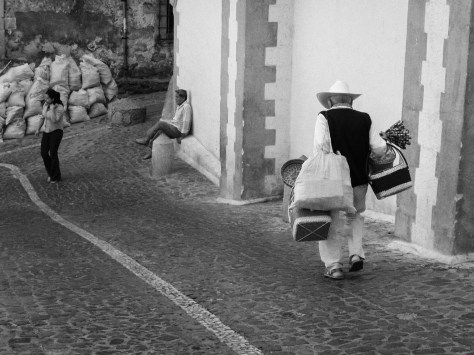 Image of an Old basket vendor, and man watching a young woman walk by. Photo by Eduardo Libby