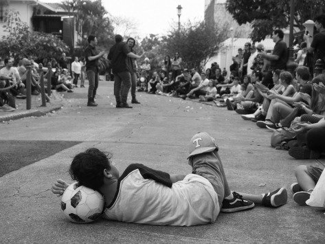 Boy watching street theater while resting his head on a soccer ball. Photo by Eduardo Libby